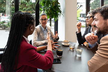 Group of young successful businesspeople having staff meeting at cafeteria, working on new strategy and ideas. Businessman and business women company owners sitting at coffee shop discussing work