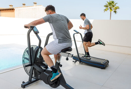 Two men exercising on a stationary bike and treadmill at home