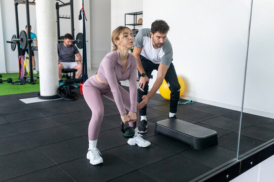 Personal trainer assists woman in modern fitness gym