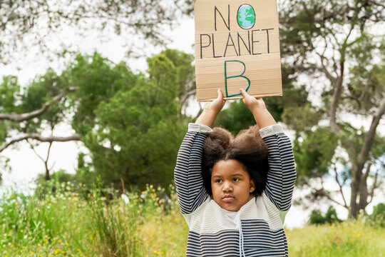 Young girl holding an environmental protest sign in park - Powered by Adobe