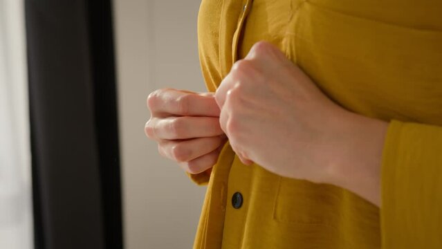 Hands close up Caucasian woman girl female influencer wear buttoning up yellow shirt clothes blogger lady prepare to work getting ready to film video blog dressing up fastening buttons fashion studio