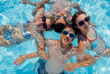 Smiling teenagers in swimsuits and sunglasses swim in the pool. A joyful group of friends is having...
