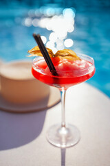 A red drink in an elegant glass with a long stem on the side of the pool. An alcoholic ice drink...