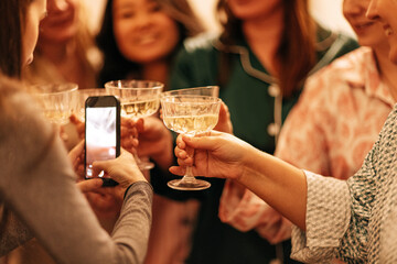 Close-up of a female hands holding a phone and toasting with glasses of champagne. A young woman...