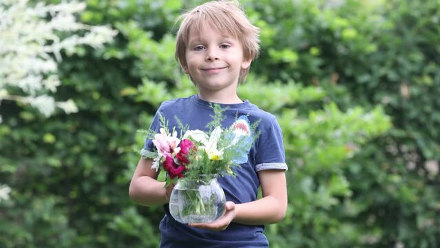 Sweet child, boy, holding vase with fild flowers in garden