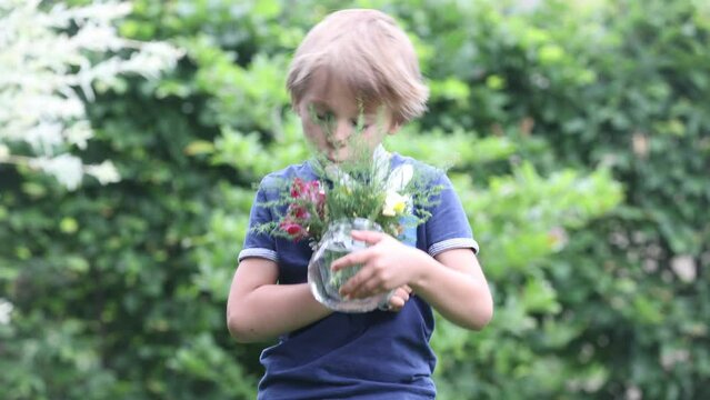 Sweet child, boy, holding vase with fild flowers in garden