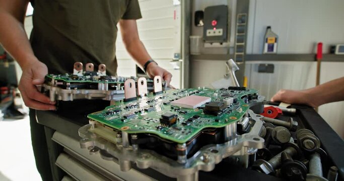 Mechanic handling and repairing an electric car engine inside a modern auto service station. Focus on circuit boards and engine components. EV repair concept. Auto Service, Electric engine