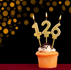 Number 126 birthday candle - Cupcake on black background with out of focus lights