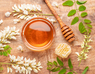 Natural organic honey in glass bowl, honey plant acacia flowers and leaves near it on wooden table....