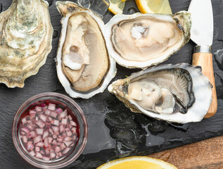 Opened raw oysters with sauce and lemon slices on gray stone serving board. Delicacy food. © volff