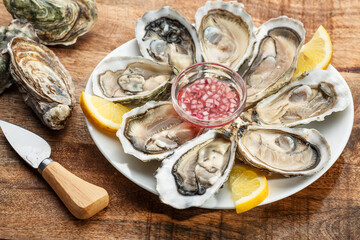 Opened raw oysters with sauce and lemon slices on plate on wooden table. Top view. © volff
