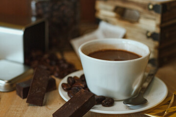 Cocoa bean tea packet in a white glass on a wooden table with chocolate chunks next to it surrounded by seeds.