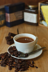 Cocoa bean tea packet in a white glass on a wooden table with chocolate chunks next to it surrounded by seeds.