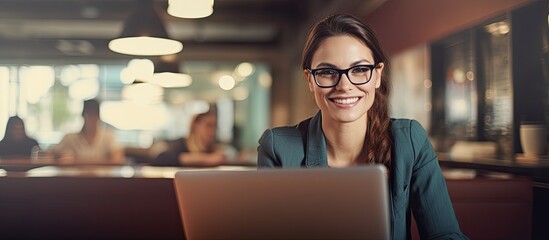 A joyful businesswoman, wearing glasses, types on a laptop inside an office, looking pleased with her accomplishments, with a backdrop of an office environment with a copy space image available.