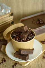 Cocoa bean tea packet in a white glass on a wooden table with chocolate chunks next to it surrounded by seeds.