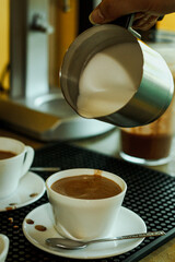 Cocoa bean tea packet in a white glass on a wooden table with chocolate chunks next to it surrounded by seeds.