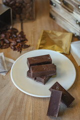 Cocoa bean tea packet in a white glass on a wooden table with chocolate chunks next to it surrounded by seeds.