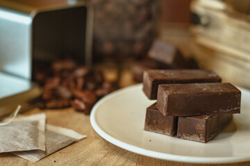 Cocoa bean tea packet in a white glass on a wooden table with chocolate chunks next to it surrounded by seeds.