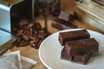 Cocoa bean tea packet in a white glass on a wooden table with chocolate chunks next to it surrounded by seeds.