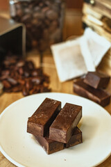 Cocoa bean tea packet in a white glass on a wooden table with chocolate chunks next to it surrounded by seeds.
