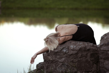 A woman is lying on a stone near the lake at wam summer evening