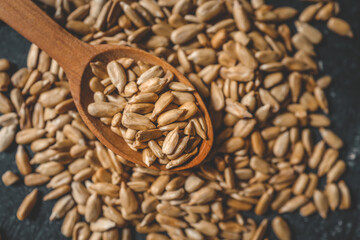 Peeled sunflower seeds on a wooden spoon, black background