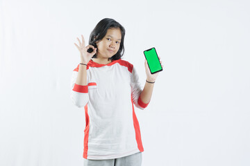Young Asian woman looks happy in Indonesian Independence Day attire. woman shows her mobile phone with green screen suitable for advertising