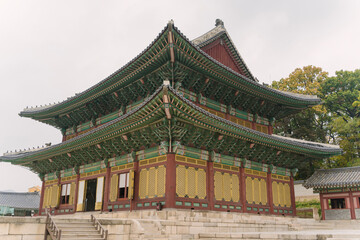 Gyeongbokgung Palace in Seoul, Korea, with visitors in traditional and modern attire walking on the spacious stone courtyard under an overcast sky.