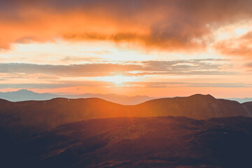 Bright orange sunset sun over mountain range. Stunning wild nature sunrise. Panoramic view of beautiful mountain landscape. Travel, tourism, adventure, concept image. Carpathian mountains, Ukraine