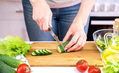 Young woman cuts cucumbers and cooking vegetable salad. Dieting and Healthy eating concept.