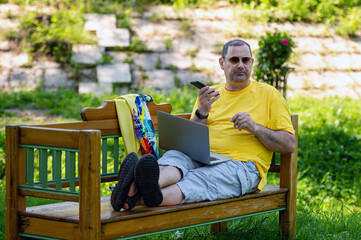 Fototapeta premium mature man with laptop and smartphone working outside in garden, green home office concept