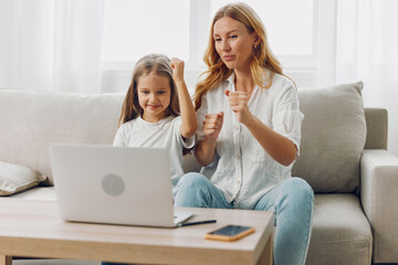 Excited woman and young girl sitting on a cozy couch raising hands in celebration while using a laptop