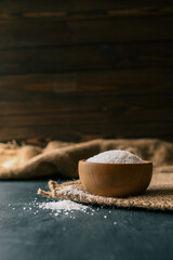 Pile of coarse sea salt in wooden bowl on black background