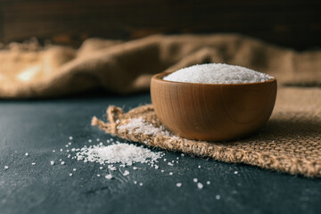 Pile of coarse sea salt in wooden bowl on black background