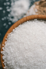 Pile of coarse sea salt in wooden bowl on black background, top view