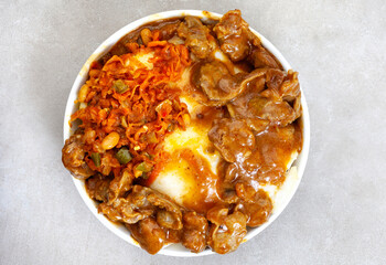 Traditional South African street food, gizzards and pap or maize meal and Chakalaka in black bowl on light grey surface 