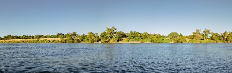 Panoramic view of the Sacramento river with lush green trees and a clear blue sky on a sunny day.