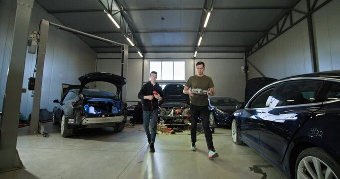 Two mechanics working on repairing electric vehicles in a modern auto repair shop. Concept of EV maintenance, service, and repair. EV repair concept. Auto Service, Electric vehicle engine maintenance