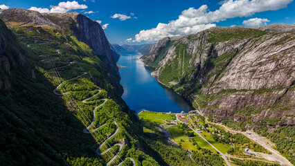 An aerial view of a winding road snaking through a breathtaking Norwegian fjord valley, with lush...