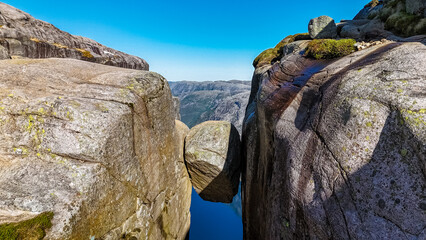 A close-up view of a large, balanced rock formation in Norway. The rock is wedged precariously...