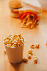 A bucket of popcorn, top-view, warm colors, light brown wooden background, flat lay, daylight macro close-up