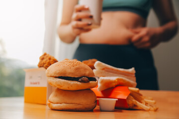 To eat or not. Cheerless plump woman looking at the burger while thinking to eat it or not