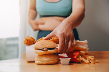 To eat or not. Cheerless plump woman looking at the burger while thinking to eat it or not