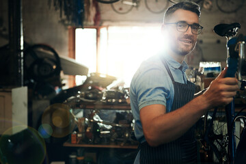 Happy man, portrait and bicycle mechanic with inspection for fix or maintenance at repair shop. Young male person, cycling technician or engineer working on bike with tools or equipment at workshop