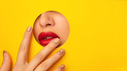 A woman face is visible through a hole in a bright yellow background. The hole frames her features,...