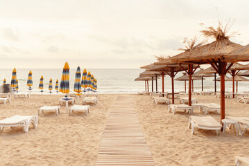 Peaceful beach with sun loungers, straw umbrellas, and a wooden walkway leading to the ocean at sunset.