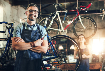 Obraz premium Man, portrait and arms crossed at work in bicycle repair shop or maintenance garage. Bike, mechanic and service with a professional handyman for startup, small business and workshop for fixing