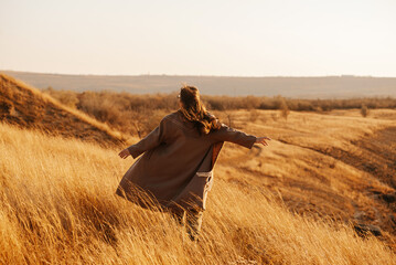 Individual in long coat with arms open wide, embracing freedom in a serene, golden field during...