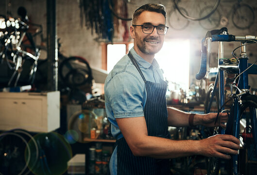Happy man, portrait or mechanic with bicycle in small business for repair, fix or maintenance. Male person, cycle technician or bike engineer working on cycling vehicle, gears or hardware at workshop
