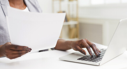 Cropped of professional black woman is handling documents at her desk in an office. The setting is sleek and organized, with a clean desk, contemporary decor